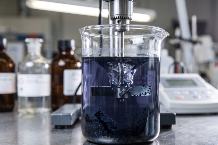 Lab beaker with dark blue disperse dye showing tar-like sediment and mechanical stirrer.