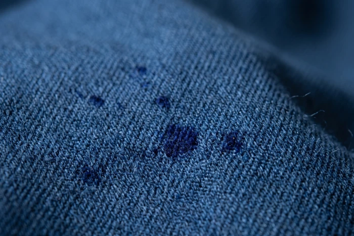 Deep blue polyester twill fabric showing dark dye specks, a common disperse dyeing fault.